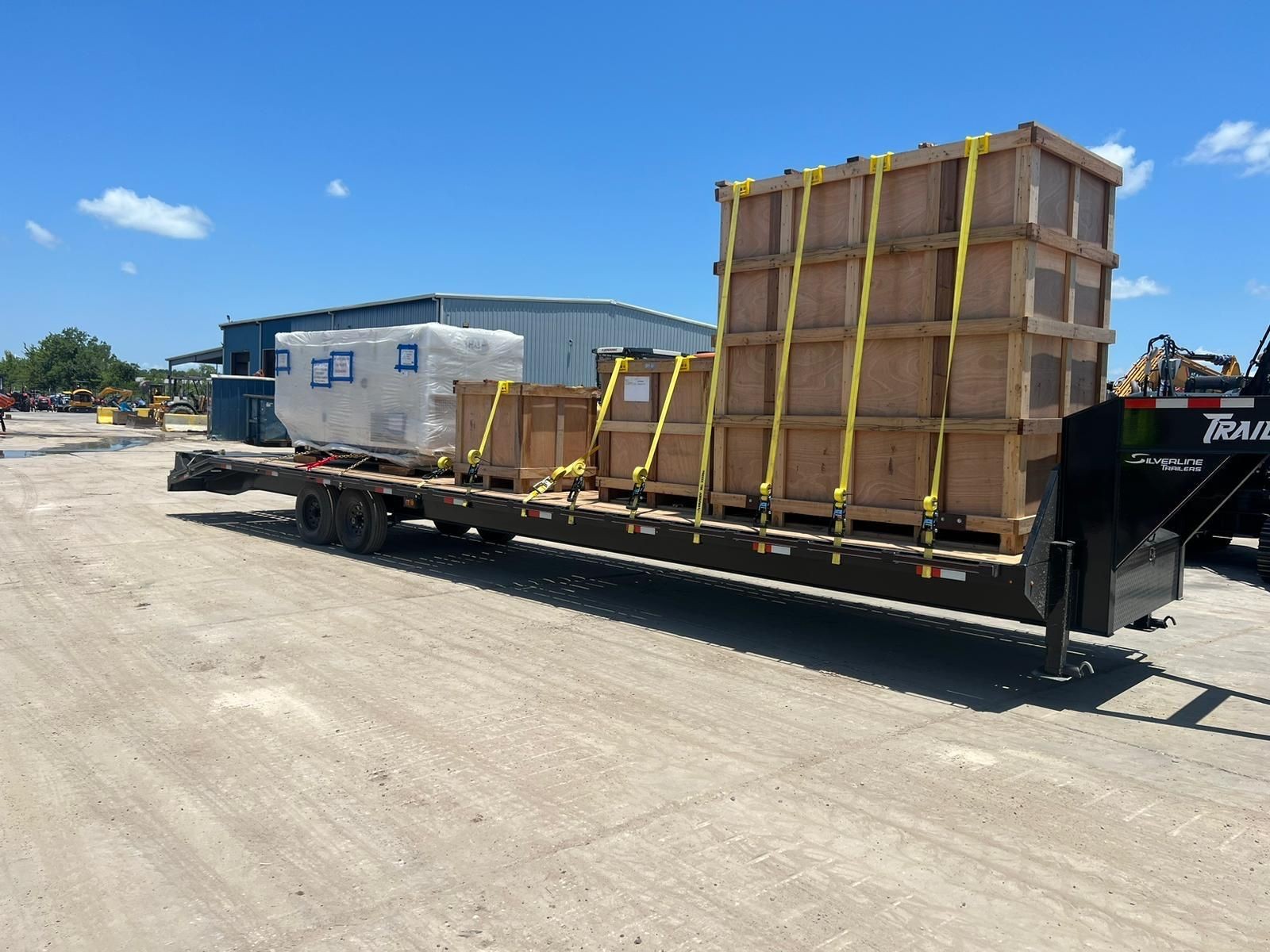 Flatbed trailer loaded with large wooden crates secured with straps, parked in an industrial area.